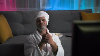 Beyaz önlüklü çekici bir adam, güzellik maskesi yapıyor, dans ediyor ve dinleniyor, televizyon izlemekten zevk alıyor. Keyfi yerinde ve üşümüş. Loş ışıklar ve pembe ve mavi bir arka planla oturma odasında.