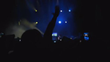 Konser müzik şovu. Sahne arkası ışıklandırmasında elini sallayan zıplayan hayran kadının karanlık silüeti. Onun güçlü duyguları var. Sarı ve mavi arka plan gösterisi, hayranların en sevdiği rock grubu çalıyor.