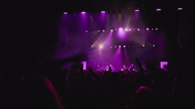 Müzik rengi ışık gösterisi. Sahne ışıklarının karşısında el sallayan hayranların karanlık silueti. Beyaz, eflatun ve mavi arka plan gösterisi, hayranların en sevdiği rock grubu sahnede