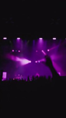 Konser müzik şovu. El sallayan hayranların karanlık silueti. Önplanda genç kadınlar yükselen eller ve güçlü duygularla dans ediyorlar. Magenta ve mavi arka plan şovu, taraftarların favorisi.