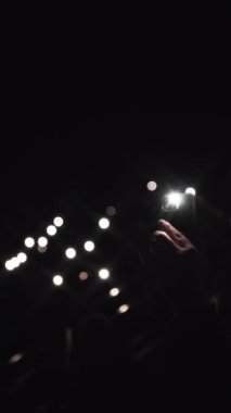Konser ışığı gösterisi. Pek çok eğlenceli insan ellerinizi kaldırıp, telefonlarınızı el fenerleriyle tutarken, onlar da rock grubunun en sevdikleri performanslarını sergilerler. Ön planda, bir kadının eli kaldırılır, telefonu tutar ve...