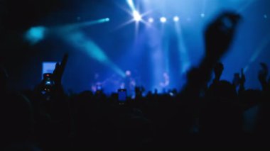 Yakın plan çekim. Dans hayranlarının karanlık silueti sahnede en sevdiği rock grubunun sahne arkası gösterisinde ellerini mavi arka planda tutuyor.