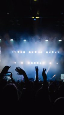 Hayranlardan oluşan bir kalabalığın kaotik hareketi favori bir rock grubunun canlı performansına. Ön planda el sallayan iki kadın ve sahne ışıklarına karşı parmakları olan iki kalp. Cyan