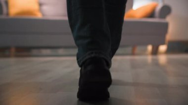 Dış giysisi ve çizmeleri olan bir kadın odanın diğer ucundan kanepeye yürür ve yol boyunca çantasıyla siyah ceketini yere bırakır. Oturma odasındaki kanepede sıcak, loş bir şekilde oturuyor.