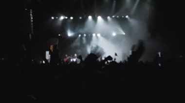 Müzikle dalgalanan hayranların karanlık silueti. Taraftarların en sevdiği rock grubunun sahne aldığı Cyan ve White Backlight Show