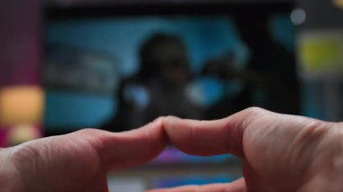 Parmakları televizyona dolanmış bir insanın ellerinden bak. Bir film izlerken ellerini ve parmaklarını ovuşturur, birbirine sarar ve masaj yapar.