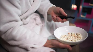 Akşam, duş aldıktan sonra, kanepede oturan beyaz cüppeli bir adam bir elinde patlamış mısır kasesi, diğer elinde uzaktan kumandayla televizyon kanallarını değiştiriyor. Şeyde...