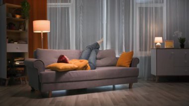 Akşamları, sarı kazak ve kot pantolon giyen mutlu, kızıl saçlı bir kadın kanepede uzanıyor. Bacakları sıcak ve loş ışıklarla oturma odasında, sarı bir yastığın üzerinde dinleniyor..