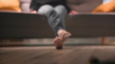 Günlük kıyafetleri, siyah kazağı, kot pantolonu ve oturma odasındaki kanepede sıcak, loş bir ışıkla oturan pembe ayakkabıları olan bir kadın. Bacaklarının yakın plan görüntüsünün netliğini bozan görüntüler yakın çekim odağı oluşturuyor.