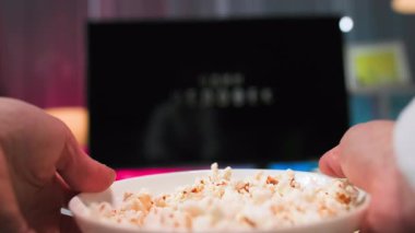 Adam oturup bir kase patlamış mısırla film izler. Televizyonun karşısında patlamış mısırı tutan bir adamın aşırı yakın çekimi. Oturma odasında pembe bir şeyle patlamış mısır yerken televizyon izliyor.