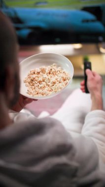 Akşamları, beyaz bornozlu bir adam bir elinde patlamış mısır, diğer elinde uzaktan kumandayla yumuşak bir kanepeye oturur. TV 'yi açar ve beyaz bir arabada patlamış mısır yerken televizyon seyreder.