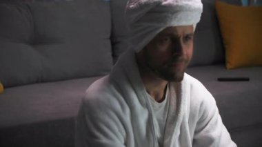 Beyaz bornozlu ve elinde patlamış mısır olan yakışıklı bir adam TV ekranında olanlara sert tepki veriyor. Ekranda olanlarla tamamen ilgiliydi. Yaşarken televizyon izliyor.