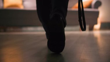 Dış giysisi ve botları olan bir kadın odanın diğer ucundan kanepeye yürür, el çantasını düşürür ve yol boyunca, oturma odasında, sıcak, loş bir ışıkla botlarını çıkartır. Yakın çekim.