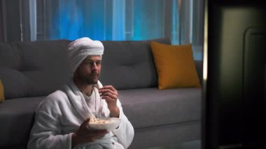 Beyaz önlüklü, yalnız, orta yaşlı bir adam patlamış mısır yiyor ve TV seyrediyor. Sonra da çılgınca kanepede uzaktan kumandayı arıyor. İstenilen kanala geçiyor ve televizyon izlemeye devam ediyor.