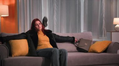 Akşamları, işten sonra giysisi ve botlarıyla yorgun, güzel kızıl saçlı bir kadın yumuşak bir kanepeye oturur, botlarını çıkarır ve dairesinde arkasına atar. Dinleniyor.