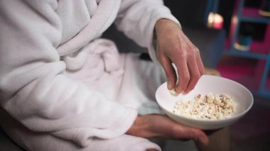 Akşam, duş aldıktan sonra, kanepede oturan beyaz cüppeli bir adam bir elinde patlamış mısır kasesi, diğer elinde uzaktan kumandayla televizyon kanallarını değiştiriyor. Şeyde...