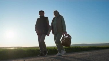 Elinde çiçek sepeti olan yaşlı bir kadın ve bir adam yeşil çayırlar ve tarlalar arasında yavaşça bir köy yolunda el ele yürüyorlar. Akşamın arka planına karşı