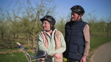 Kısa bir mola sırasında, yaşlı bir çift iki koltuklu bisiklete binen bir gezi hakkındaki canlı izlenimlerini paylaşıyor. Yaşlı kadın kocasının yanında duruyor ve elinde bir kır çiçeğini tutuyor.