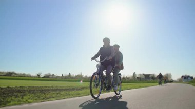 İki koltuklu bisiklet süren yaşlı bir çift, torunlarıyla birlikte yeşil tarlaların arasında şehir dışında geziyorlar. Arkaplan güneşinde alçaktan görüntüyü çek