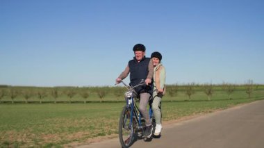 Çift yeşil çayırlar arasında bir köy yolu boyunca iki koltuklu bir bisiklet sürüyor. Onlar sıcak bahar güneşli havada güzel bir kırsal alanda bir yol boyunca at sürüyorlar. Bir sürü izlenim ediniyorum.