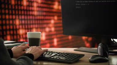 Takım elbiseli bir kadın masa başında oturup bilgisayar klavyesine yazı yazıyor. Klavye çerçevenin ortasında, üzerinde insan eli dinleniyor. Masanın üzerinde bir fincan kahve, bir fare ve kulaklıklar var.