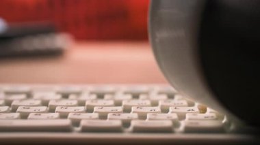 Kadın klavyeye yazı yazıp üstüne çay döküyor. Arka planda bir masa beyaz bir klavye. Renk şeması, siyah ve beyaz aksanlı, kahverengi ve turuncu gibi sıcak tonları içerir. Genel olarak.