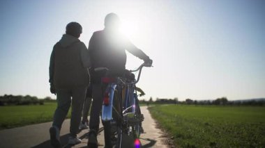 Bir kır bisikleti sürüşünden sonra, yorgun bir aile yeşil tarlaların arka planına karşı eve döner ve şehir dışındaki bir köy yolunda birlikte yürürler. Güneşe, yetişkinlere ve çocuklara karşı