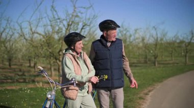 Kısa bir mola sırasında, yaşlı bir çift iki koltuklu bisiklete binen bir gezi hakkındaki canlı izlenimlerini paylaşıyor. Yaşlı kadın kocasının yanında duruyor ve elinde bir kır çiçeğini tutuyor.