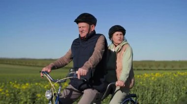 Aktif bir yaşam tarzı sürdüren yaşlı bir çift iki koltuklu bisiklette spor yapıyor. Onlar sıcak bahar güneşli havada güzel bir kırsal alanda bir yol boyunca at sürüyorlar. Birbirleriyle konuşuyorlar.