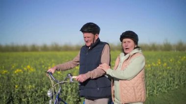 Yaşlı bir adam ve kadın kırsal bir yolda yürüyor sohbet ediyor ve etraflarındaki kır çiçeklerinin tadını çıkarıyorlar. Adam bisikletle yürüyor, kadın da erkeğin elini tutuyor. Orta uzunlukta..