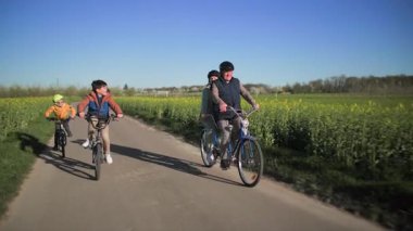 İki koltuklu bisiklete binen yaşlı bir çift ve torunları tarlalar arasında bir kır yolu boyunca bisiklet sürüyor, ve ılık bahar güneşinin ışınlarında yeşil çayırlar 