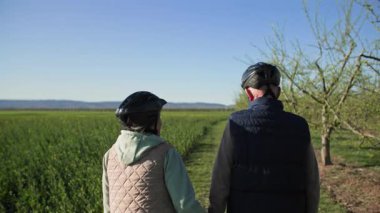 Şehrin dışındaki bir dinlenme tesisinde, yaşlı bir çift bir tarlanın kenarındaki yeşil çimlerde geziniyor, meyve ağaçlarının yanından geçiyor. Erkek ve kadın el ele tutuşuyorlar. Görüntüler şu taraftan çekiliyor: