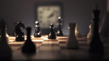 Bir adam satranç oyununa dalmış, önünde bir satranç tahtasıyla masada oturuyor. Eli, beyaz bir veziri ustalıkla hokkabazlık yaparak bir sonraki hamlesinin stratejisini düşünüyor.