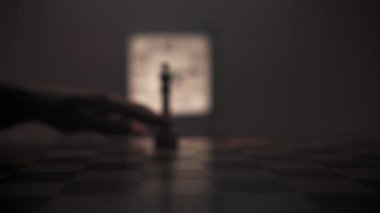 Loş bir odada, bir adam dikkatle satranç taşını tahta bir satranç tahtasının ön planına eliyle taşır. Sahnenin ana renkleri kahverengi ve siyah tonlarıdır. Ortam iletir