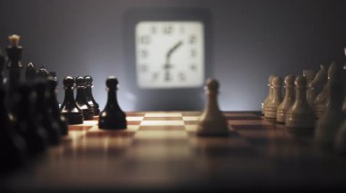 Büyük yakın çekim. Hızla değişen bir çevre ve taşların düzenlendiği bir satranç oyunu. Satranç tahtasının yanında saati gösteren bir saat var. Sahne sıcacık ışıkla aydınlatılıyor.