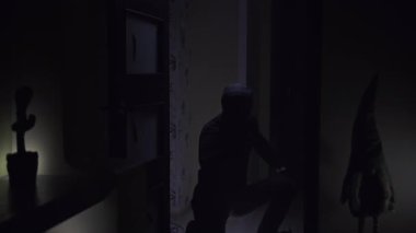 Loş bir ışığın aydınlattığı karanlık bir odanın girişinde tek başına duran bir adam. Siyah bir kapüşonlu giyiyor, gizemli ve uğursuz bir atmosfer yaratıyor. Adam elinde bir el feneri tutuyor ve başlıyor.