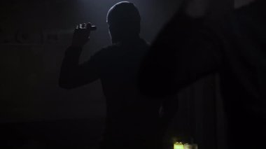 Siyah giyinmiş ve maske takmış korkmuş bir adam sırtı aynaya dönük duruyor ve tehlikeyi belirlemek için fener ışınıyla karanlık bir odanın çevresini araştırıyor. Oda karanlık.