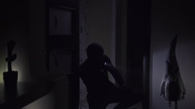 Karanlık bir odanın girişinde siyahlı bir adam feneri açar ve odayı inceler, sonra yavaşça ve sessizce içeri girer. Oda loş bir şekilde aydınlatılmış, tek ışık kaynağı el feneri.