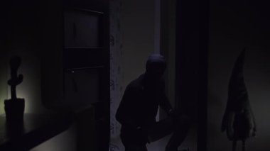 Siyahlı adam bir dizinin üzerine çok yumuşak bir şekilde oturur feneri açar ve karanlık odayı keşfeder sonra karanlıkta yükselir ve kaybolur. Çekim bir gizem ve entrika hissi veriyor.