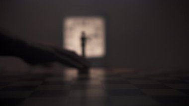 Loş bir odada, bir adam dikkatle satranç taşını tahta bir satranç tahtasının ön planına eliyle taşır. Sahnenin ana renkleri kahverengi ve siyah tonlarıdır. Ortam iletir