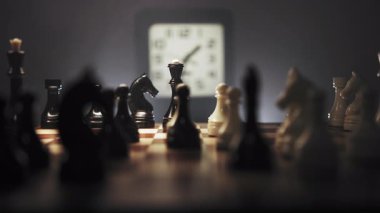 Büyük yakın çekim. Hızla değişen bir çevre ve taşların düzenlendiği bir satranç oyunu. Satranç tahtasının yanında saati gösteren bir saat var. Sahne sıcacık ışıkla aydınlatılıyor.