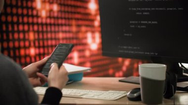 Ofis masasındaki bir programcı aktif olarak bir telefona bilgi aktarıyor ve bu da bilgisayar monitöründe gösteriliyor. Masanın üzerinde bir fincan kahve, bir fare ve kulaklıklar var. Şeyde...