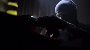 Elinde fener olan maskeli ve siyah giysili bir hırsız karanlık bir odada şifonyer çekmecesi açıyor. Elbiselerini çekmeceden çıkarıp değerli eşyalar arıyor. Değerli bir şey bulamayınca, adam kapatıyor.