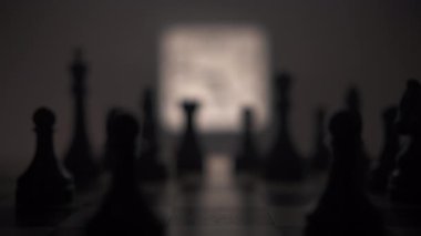 Bir satranç tahtasının çok sayıda siyah taşla yakın çekimi, ortaya bir insan eli, oyunun yeni koşullarını dikte eden beyaz bir papaz taşını koyar. Satranç tahtasının arka planında parlak bir...