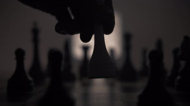 Bir satranç tahtasının çok sayıda siyah taşla yakın çekimi ve tahtanın ortasına bir insan eli beyaz bir papaz taşını yerleştirir. Satranç tahtasının arka planında parlak bir siyah beyaz var.