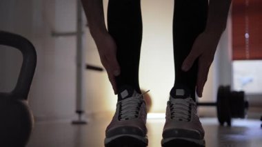 Spor ayakkabılı bir sporcu, vücudunu esnetiyor ve gevşetiyor. Önünde bir kettlebell, arkasında da yerde bir dambıl var. Spor salonundaydı ve...