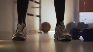 Spor ayakkabılı bir sporcu bacaklarını ısıtır ve kettlebell ile güç egzersizleri yapar. Spor yaptığı bir fitness merkezindeymiş. Arka planda birkaç dambıl ve...