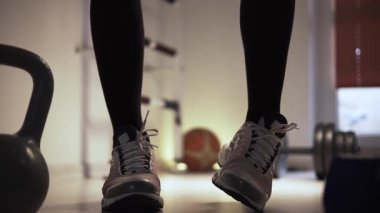 Bir adam spor salonunun zemininde ısınıyor ve antrenmana hazırlanıyor. Adam spor ayakkabısı giyiyor. Zıplama hareketlerinden sonra kontrol ediyor ve ayarlıyor. Erkek ayağının yanında...