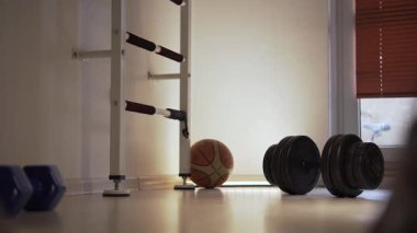 At the gym, a man in sneakers takes a few steps forward to the dumbbells, slows down, thinking next actions. He is in a fitness center where he is doing a workout. There are several dumbbells and a