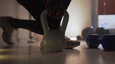 Spor salonundaki bir sporcu diz çöker, bir kettlebell alır ve onunla birlikte ayağa kalkar, sonra tekrar diz çöker ve kettlebell 'i yere yerleştirir. Spor yaptığı bir fitness merkezinde kalıyor. Şeyde...